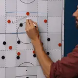 Trainer erklärt eine 4-1-3-2 Formation auf einem Taktikboard. Rote und schwarze Magnete stellen Spieler dar.