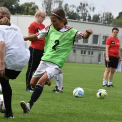 Mädchen im **Jugend Fußball** Training üben Dribblings. Ein Mädchen mit grüner Weste und der Nummer 2 am Ball.
