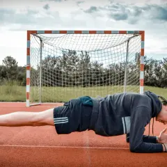 Mann in Unterarmstütz, um den Rumpf zu stabilisieren, vor einem Fußballtor.