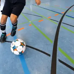 Ein Spieler übt Dribblings auf dem Hallenboden, die Linien markieren die Futsal Positionen.