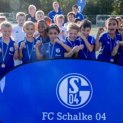 Junge Fußballer der Schalke U10 jubeln mit Medaillen vor einem Banner des FC Schalke 04.