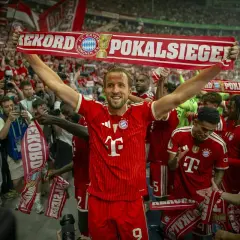 Harry Kane feiert mit seinen Teamkollegen und Fans einen Pokalsieg. Die Spieler halten ein Banner mit der Aufschrift "Rekord Pokalsiege".