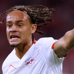 Xavi Simons, mit Dreadlocks und einem Stirnband, zeigt aufgeregt auf etwas, während er das RB Leipzig Trikot trägt.