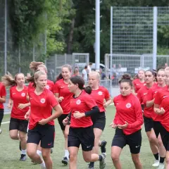 Eine Gruppe junger Fußballerinnen der u17 Juniorinnen im roten Trikot läuft auf einem Kunstrasenplatz.