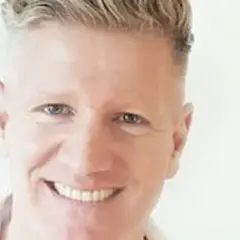 Ein Mann mit blondem Haar lächelt. Er könnte ein Sportpsychologe sein, der Athleten hilft, ihre mentale Stärke zu entwickeln.