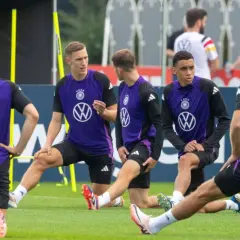 Fußballer in violetten Trikots dehnen ihre Wade auf dem Trainingsplatz.