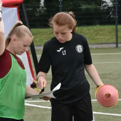 Zwei junge Fußballerinnen besprechen den Trainingsplan. Die eine hält einen Zettel, die andere einen Trainingskegel. Perfekte f jugend spielzeit.