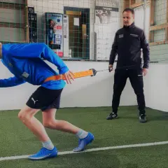 Junge trainiert mit Widerstandsband für schnelles Krafttraining, Coach beobachtet.