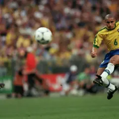 Roberto Carlos schuss geschwindigkeit: Der Brasilianer im gelben Trikot schießt den Ball mit voller Wucht. Ein Franzose im blauen Trikot beobachtet die Szene.