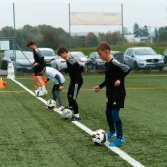 Jungs beim Kinderfußball Training üben mit Bällen auf dem Kunstrasen.
