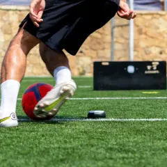 Fußballer trainiert seine reaktionsschnelligkeit mit einem Ball und einem kleinen Trainingsgerät auf Kunstrasen.
