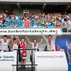 Familie jubelt bei einem Spiel der RB Leipzig U11. Die Fans tragen Trikots und Schals des Vereins.
