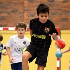 Jungen in Sporttrikots spielen Staffelspiele mit Ball in einer Sporthalle.