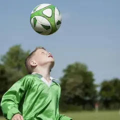 Junge im grünen Trikot übt den Kopfball. Der Ball schwebt über ihm, bereit für den perfekten Treffer.