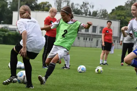 Mädchen im **Jugend Fußball** Training üben Dribblings. Ein Mädchen mit grüner Weste und der Nummer 2 am Ball.