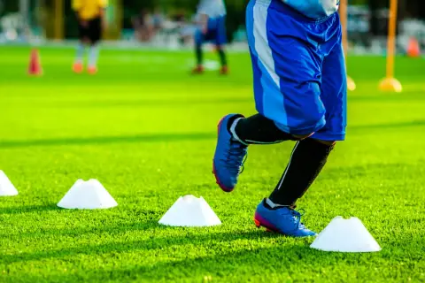 Ein Fußballer absolviert ein intensives plyometrisches Training auf einem grünen Kunstrasenplatz, um seine Sprungkraft zu verbessern.