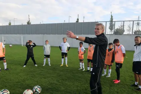 Trainer erklärt jungen Fußballern auf dem Feld Taktiken, die für ein DFB Duales Studium relevant sein könnten.