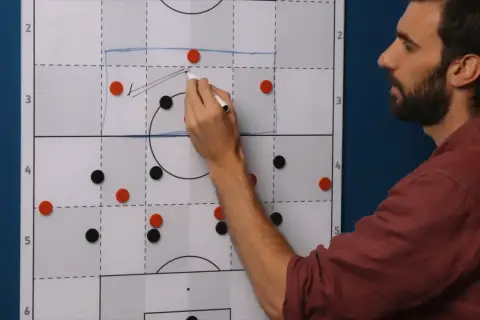 Trainer erklärt eine 4-1-3-2 Formation auf einem Taktikboard. Rote und schwarze Magnete stellen Spieler dar.