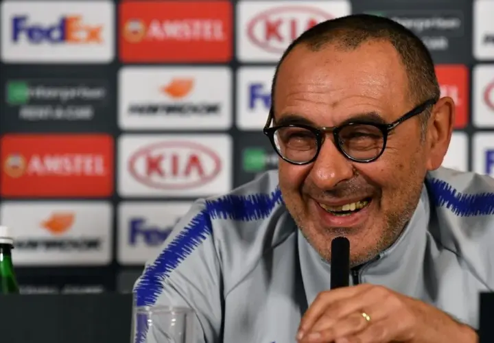 Lachender Sarri Trainer mit Brille und blauem Kragen. Hinter ihm Logos von Sponsoren.