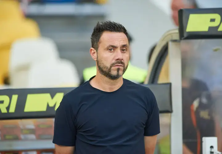 Roberto De Zerbi, mit seinem charakteristischen Blick, steht im Stadion. Seine bisherigen Trainerstationen prägen seine Laufbahn.