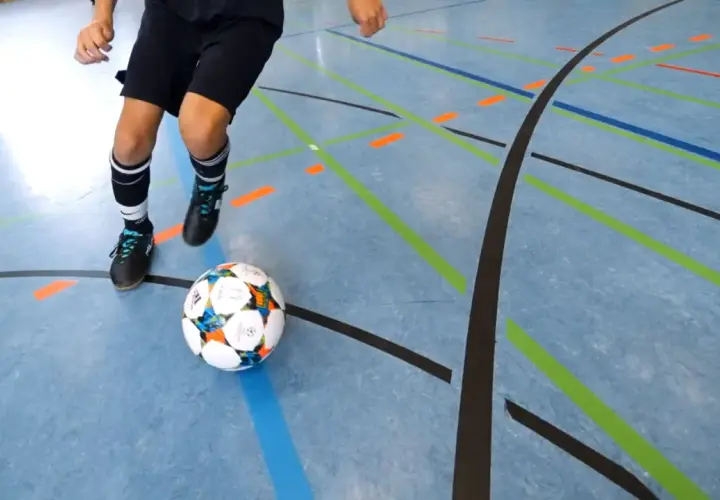Ein Spieler übt Dribblings auf dem Hallenboden, die Linien markieren die Futsal Positionen.