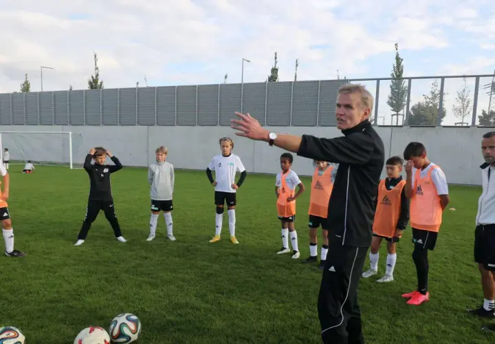 Trainer erklärt jungen Fußballern auf dem Feld Taktiken, die für ein DFB Duales Studium relevant sein könnten.