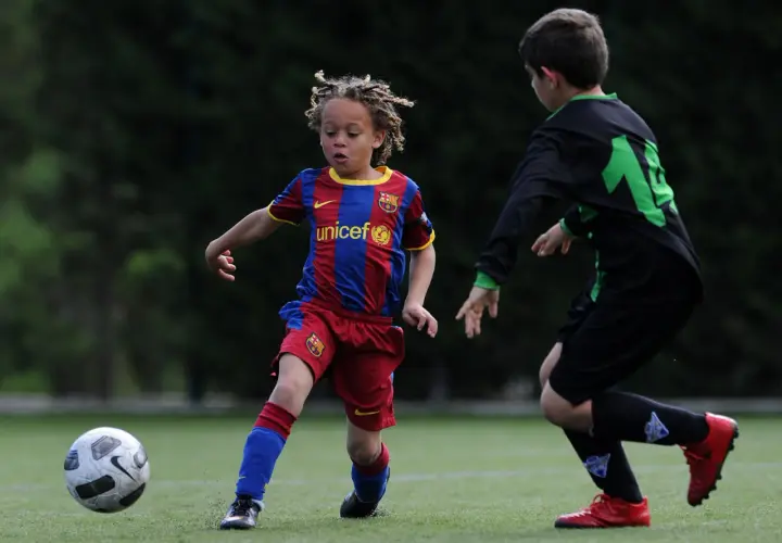 Ein junger Fußballer, vielleicht ein **Xavi Simons Kind**, dribbelt im Barcelona-Trikot auf dem Feld.