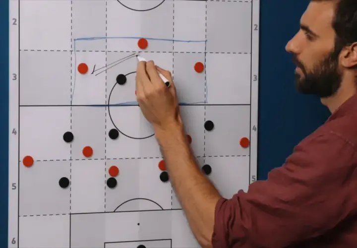 Trainer erklärt eine 4-1-3-2 Formation auf einem Taktikboard. Rote und schwarze Magnete stellen Spieler dar.