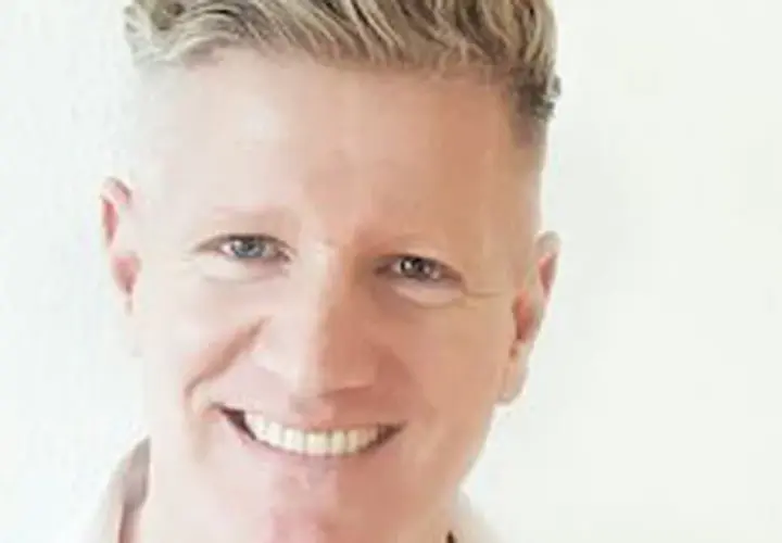 Ein Mann mit blondem Haar lächelt. Er könnte ein Sportpsychologe sein, der Athleten hilft, ihre mentale Stärke zu entwickeln.