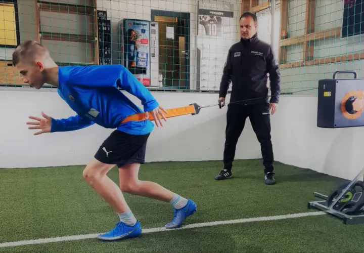 Junge trainiert mit Widerstandsband für schnelles Krafttraining, Coach beobachtet.
