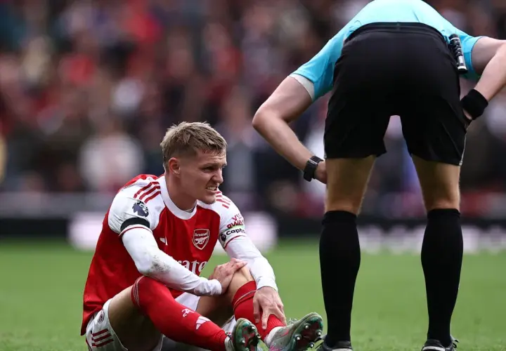 Martin Ødegaard sitzt verletzt auf dem Rasen, während ein Schiedsrichter ihn beobachtet.