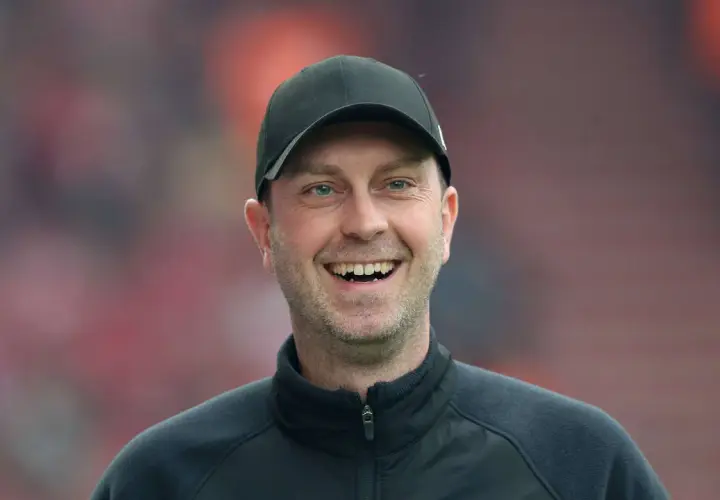 Lachender rb leipzig trainer mit schwarzer Kappe und Trainingsjacke vor unscharfem Publikum.