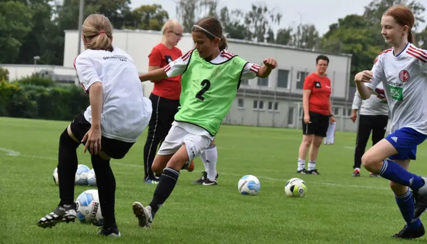 Mädchen im **Jugend Fußball** Training üben Dribblings. Ein Mädchen mit grüner Weste und der Nummer 2 am Ball.