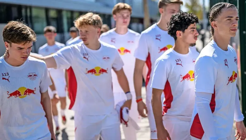 Junge Fußballer des RB Leipzig U12 Teams in weißen Trikots mit dem Bullen-Logo gehen gemeinsam.