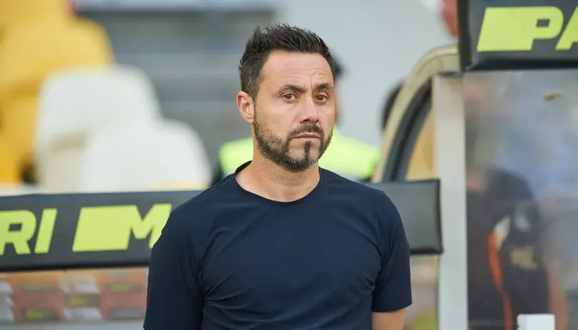 Roberto De Zerbi, mit seinem charakteristischen Blick, steht im Stadion. Seine bisherigen Trainerstationen prägen seine Laufbahn.
