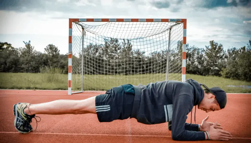 Mann in Unterarmstütz, um den Rumpf zu stabilisieren, vor einem Fußballtor.