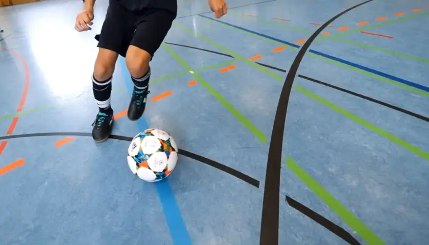 Ein Spieler übt Dribblings auf dem Hallenboden, die Linien markieren die Futsal Positionen.