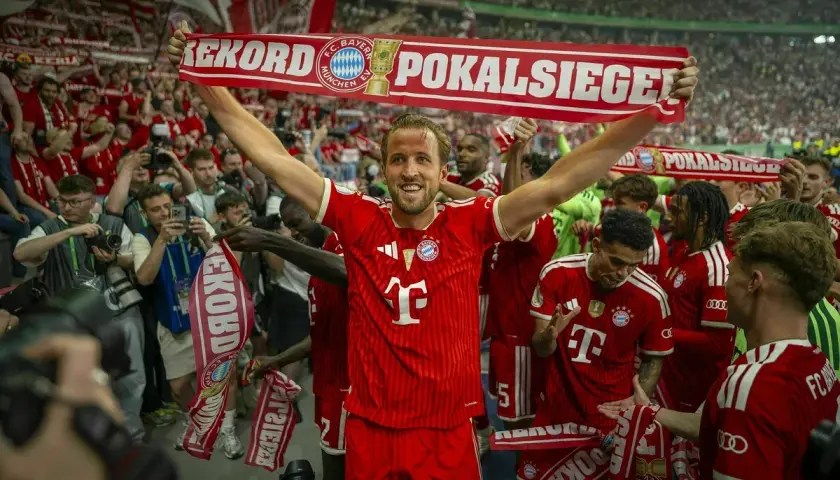 Harry Kane feiert mit seinen Teamkollegen und Fans einen Pokalsieg. Die Spieler halten ein Banner mit der Aufschrift "Rekord Pokalsiege".