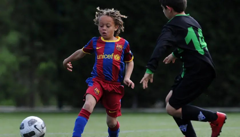 Ein junger Fußballer, vielleicht ein **Xavi Simons Kind**, dribbelt im Barcelona-Trikot auf dem Feld.