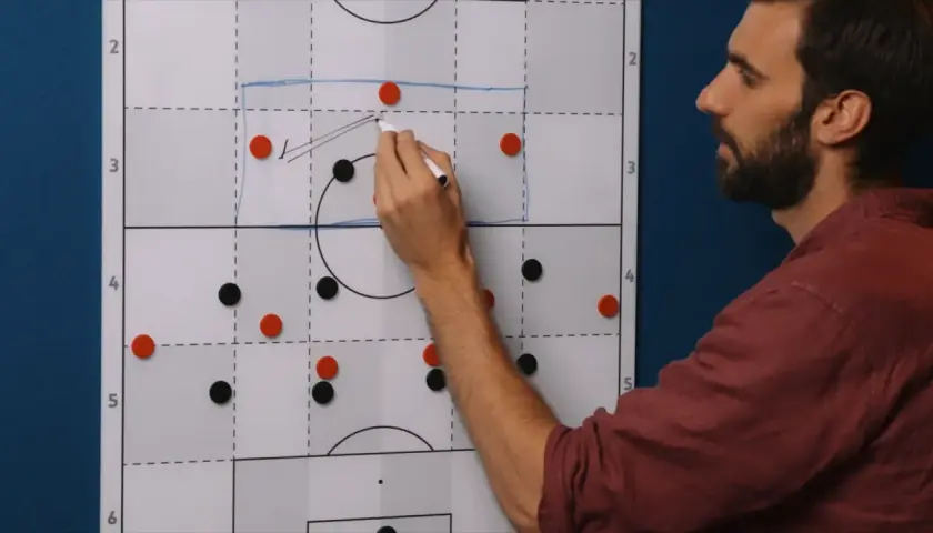 Trainer erklärt eine 4-1-3-2 Formation auf einem Taktikboard. Rote und schwarze Magnete stellen Spieler dar.