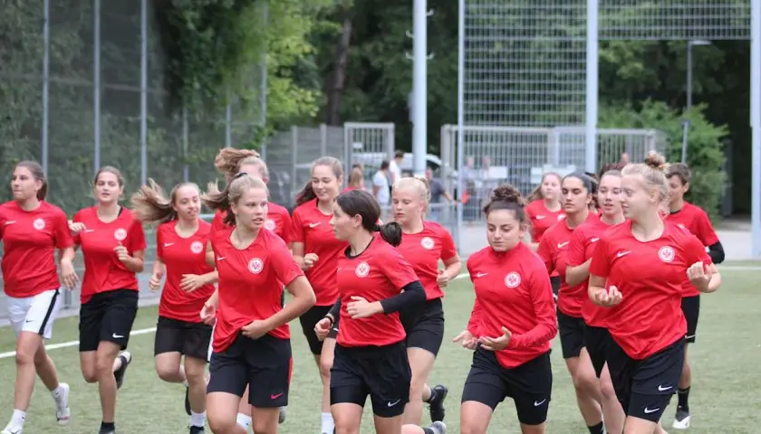 Eine Gruppe junger Fußballerinnen der u17 Juniorinnen im roten Trikot läuft auf einem Kunstrasenplatz.