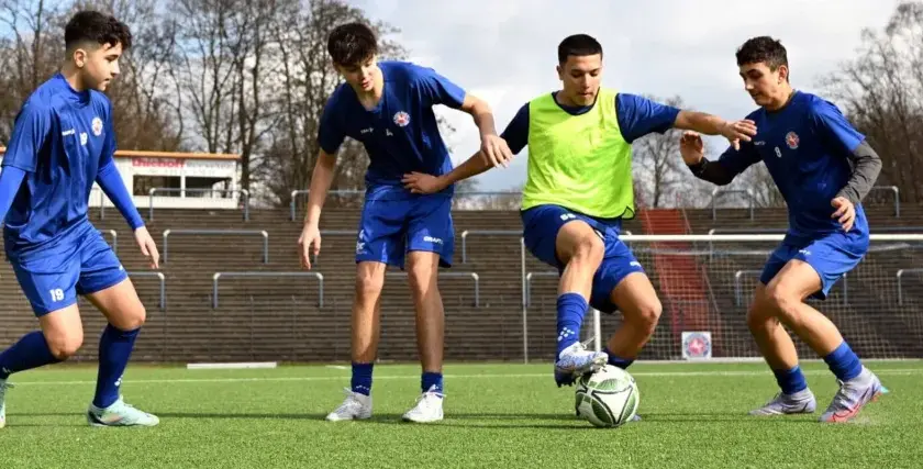 Vier junge Fußballer im C-Jugend-Training üben auf dem Kunstrasen. Einer dribbelt den Ball, die anderen verteidigen.