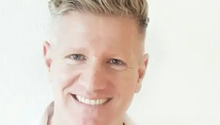 Ein Mann mit blondem Haar lächelt. Er könnte ein Sportpsychologe sein, der Athleten hilft, ihre mentale Stärke zu entwickeln.