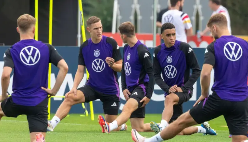 Fußballer in violetten Trikots dehnen ihre Wade auf dem Trainingsplatz.