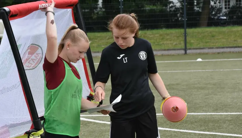 Zwei junge Fußballerinnen besprechen den Trainingsplan. Die eine hält einen Zettel, die andere einen Trainingskegel. Perfekte f jugend spielzeit.