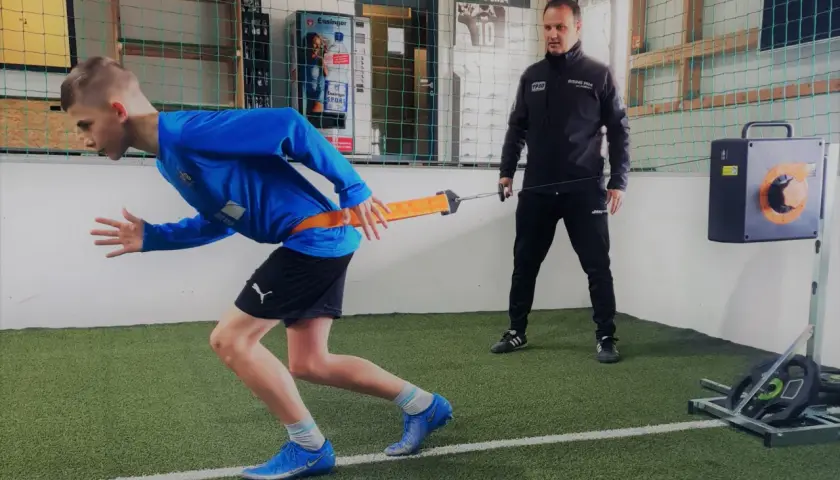 Junge trainiert mit Widerstandsband für schnelles Krafttraining, Coach beobachtet.