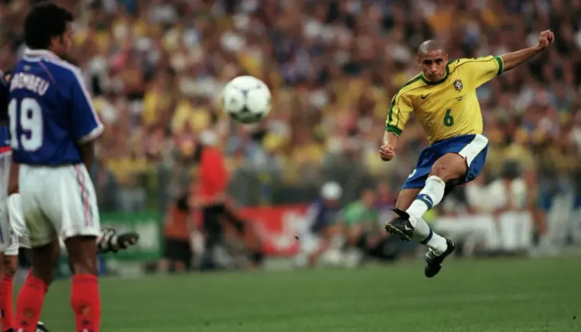 Roberto Carlos schuss geschwindigkeit: Der Brasilianer im gelben Trikot schießt den Ball mit voller Wucht. Ein Franzose im blauen Trikot beobachtet die Szene.