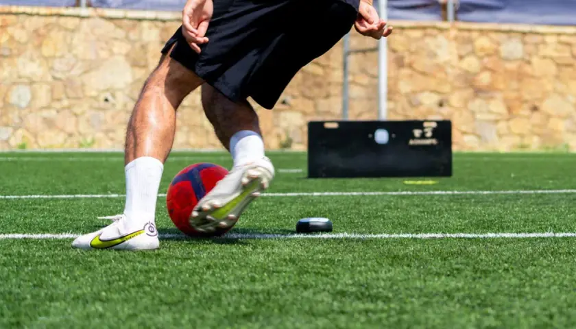 Fußballer trainiert seine reaktionsschnelligkeit mit einem Ball und einem kleinen Trainingsgerät auf Kunstrasen.