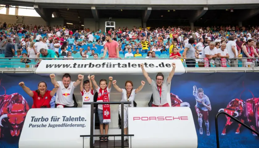 Familie jubelt bei einem Spiel der RB Leipzig U11. Die Fans tragen Trikots und Schals des Vereins.