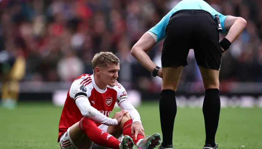 Martin Ødegaard sitzt verletzt auf dem Rasen, während ein Schiedsrichter ihn beobachtet.